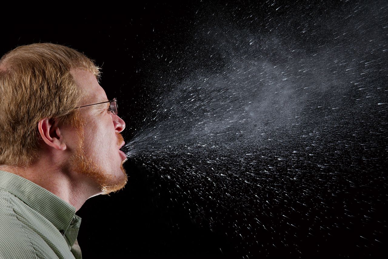 A man sneezing showing droplets spraying into the air.