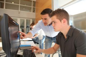 Male teacher helps a student work on a computer. 