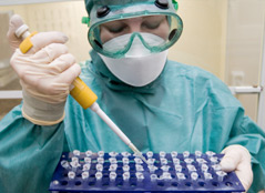 A female scientist in protective clothing adds chemicals to small test tubes.