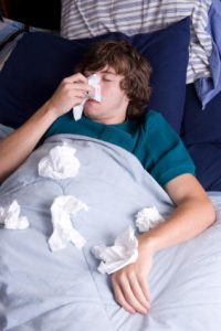 Male teen lying in bed blowing his nose.